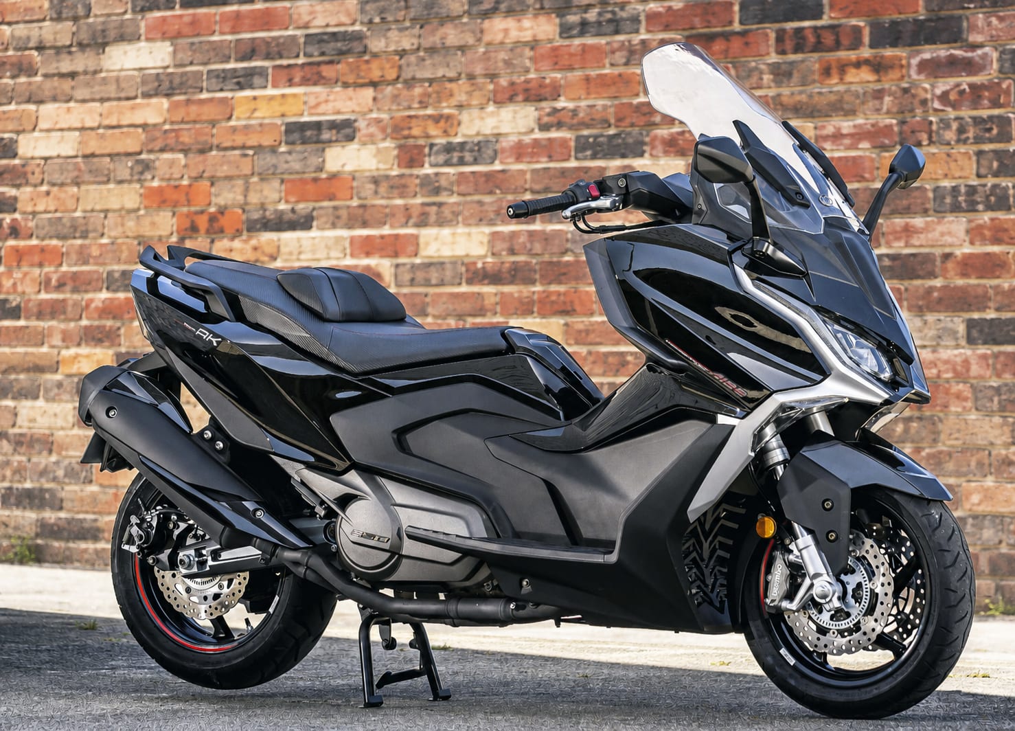 Complete List of All Motorcycles with Cornering ABS/IMU (2026) 20 Black Kymco AK 550i Premium maxi-scooter in front of a mixed-colour brick wall
